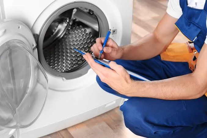 Technician writing service notes beside a front-loading washer