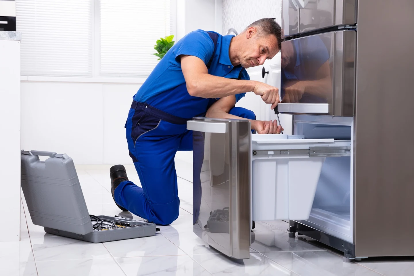 Technician inspecting an open refrigerator with a screwdriver