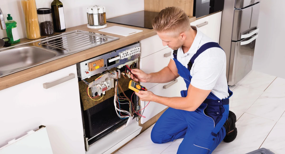 Technician testing a dishwasher electrical panel with a multimeter